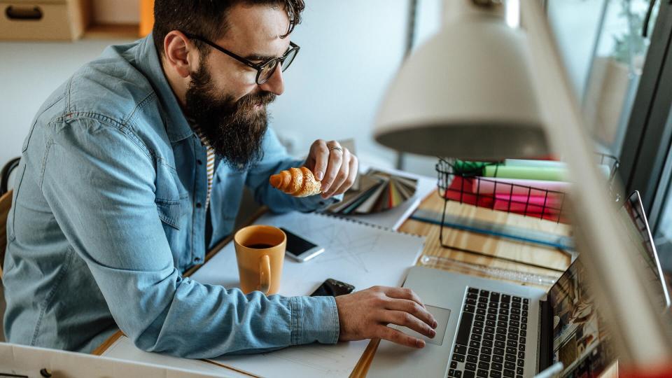 Bearded man eating in office.