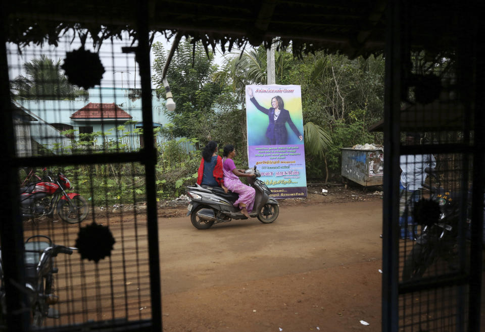 Village women ride past a banner featuring U.S. Vice President-elect Kamala Harris in Thulasendrapuram, the hometown of Harris' maternal grandfather, south of Chennai, Tamil Nadu state, India, Wednesday, Jan. 20, 2021. A tiny, lush-green Indian village surrounded by rice paddy fields was beaming with joy Wednesday hours before its descendant, Kamala Harris, takes her oath of office and becomes the U.S. vice president. (AP Photo/Aijaz Rahi)