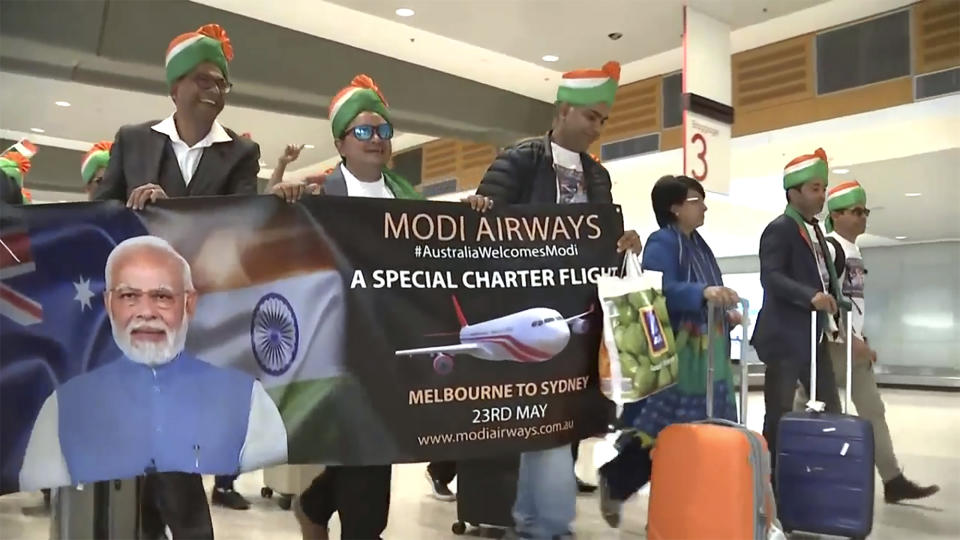 In this image made from video, Indian expats wearing traditional dress walk through Sydney Airport, carrying Modi Airways banner, in Sydney, Australia, Tuesday, May 23, 2023. Hundreds of Indian Australians have arrived on a charter flight from Melbourne to Sydney to attend an community event for visiting Prime Minister Narendra Modi. (Australian Broadcasting Corp. via AP)