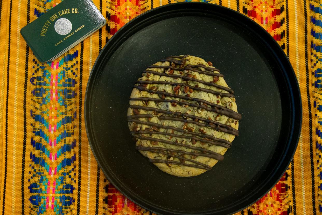 A giant gourmet cookie sits on a table at Pretty One Cake Co. Friday, Aug. 25, 2023. It's a chocolate chip cookie mixed with pecans and drizzled in chocolate.