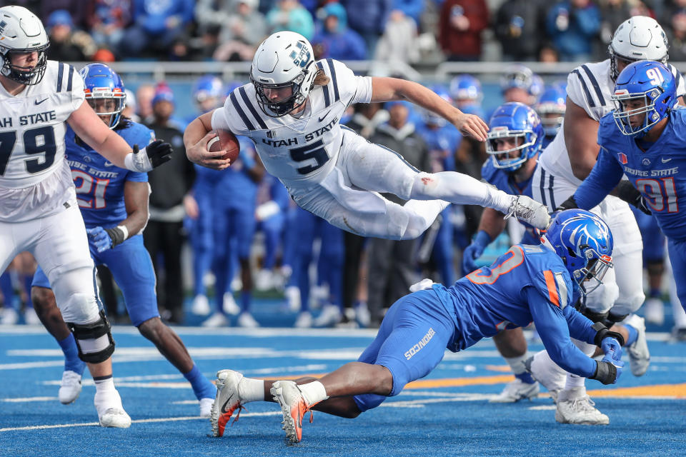 BOISE, ID - NOVEMBER 25: Quarterback Cooper Legas #5 of the Utah State Aggies takes to the air to avoid the tackle of safety Seyi Oladipo #23 of the Boise State Broncos during second half action at Albertsons Stadium on November 25, 2022 in Boise, Idaho. Boise State won the game 42-23. (Photo by Loren Orr/Getty Images)