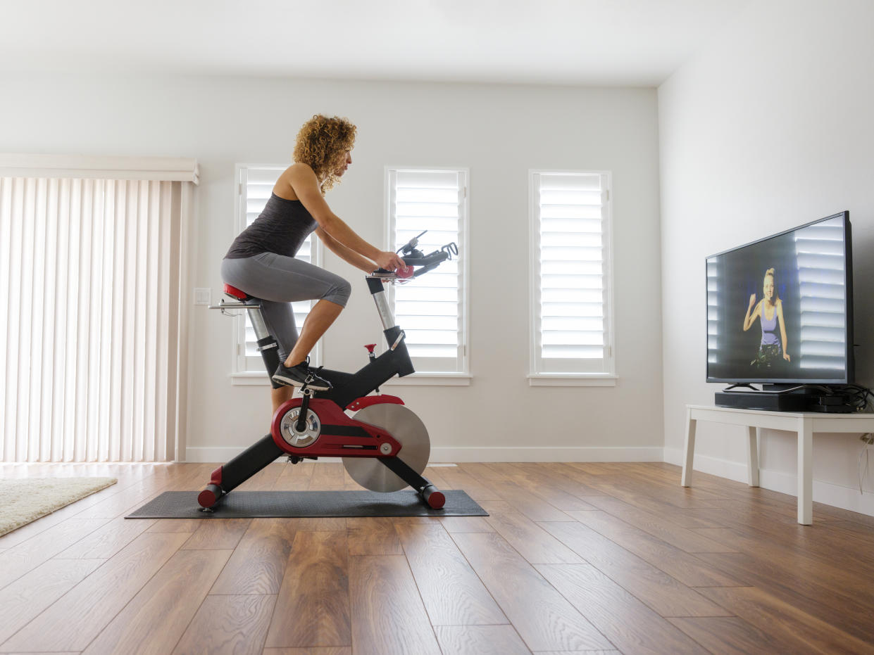 A woman exercising on a spin bike using an online instructor inside a home.