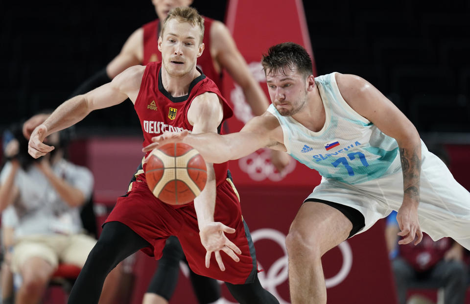 Germany's Niels Giffey (5), left, and Slovenia's Luka Doncic (77) fight for a loose ball during men's basketball quarterfinal game at the 2020 Summer Olympics, Tuesday, Aug. 3, 2021, in Saitama, Japan. (AP Photo/Charlie Neibergall)