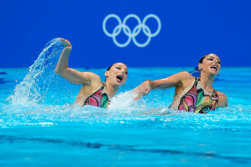 Two swimmers swimming at an angle and half out the water, with mouths wide open