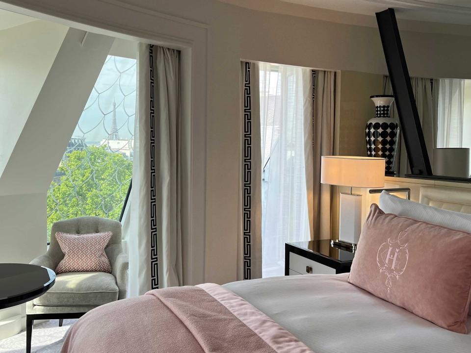 A hotel room with a bed, chair, and the Eiffel Tower seen in the distance through the window.