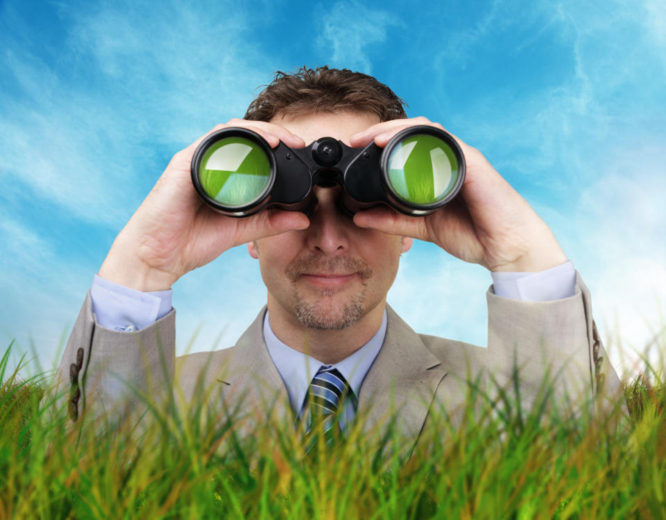 Businessman standing in tall grass looking through binoculars.