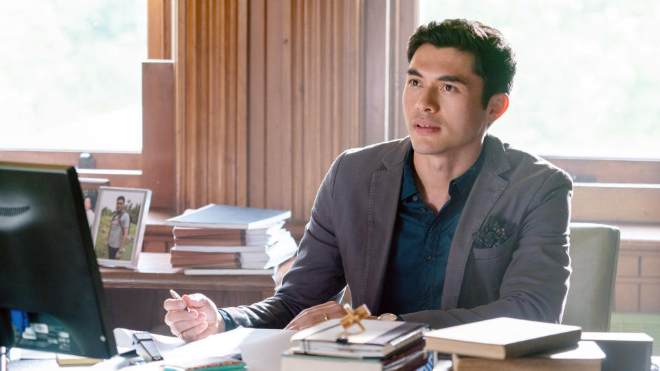 Henry in a blazer at a desk with a computer, looking thoughtful