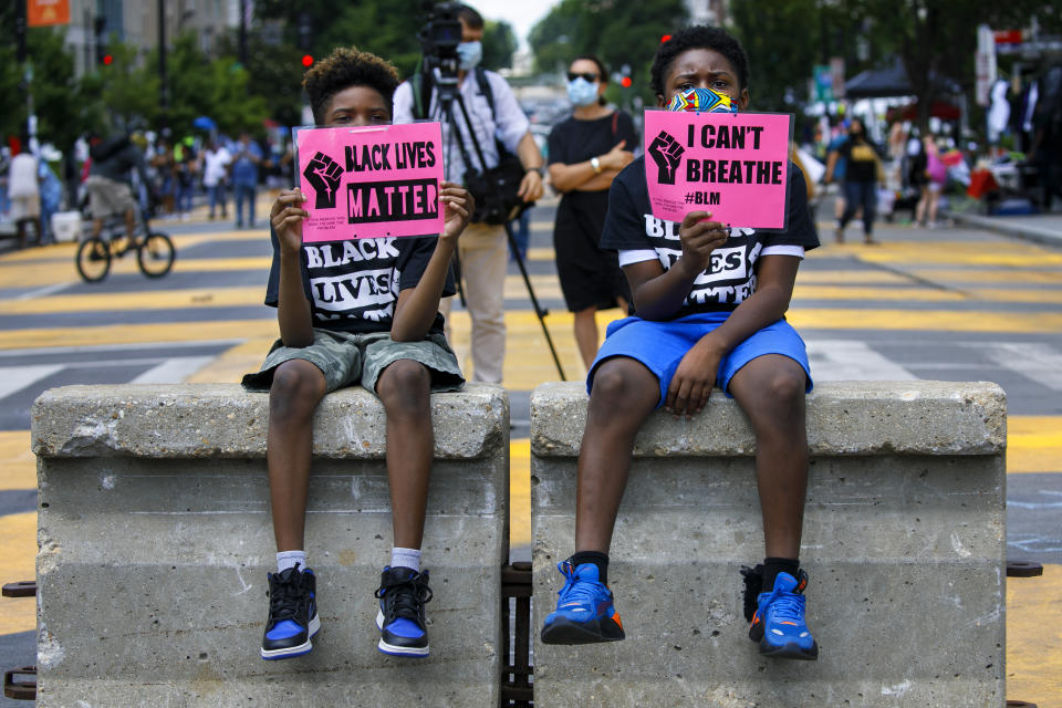 FILE - In this June 24, 2020, file photo, Tyshawn, 9, left, and his brother Tyler, 11, right, of Baltimore, hold signs saying "Black Lives Matter" and "I Can't Breathe" as they sit on a concrete barrier near a police line as demonstrators protest along a section of 16th Street that has been renamed Black Lives Matter Plaza in Washington. Thousands of Black activists from across the U.S. will hold the 2020 Black National Convention on Aug. 28, 2020, via livestream to produce a new political agenda that builds on the protests that followed George Floyd’s death. Organizers of the gathering shared their plans with The Associated Press on Wednesday, July 1, ahead of an official announcement. (AP Photo/Jacquelyn Martin, File)