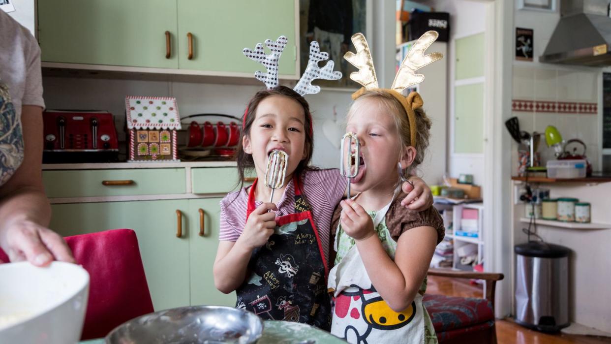 girls hugging and tasting mix from egg beater whilst preparing food for christmas