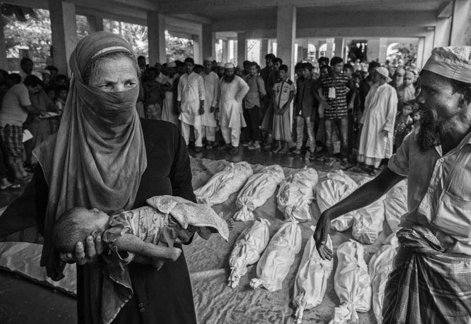 A woman carries the body of a Rohingya refugee baby. Others are seen wrapped in white sheets prior to burial after they died when their boat capsized while fleeing Myanmar on Sept. 29 in Cox's Bazar, Bangladesh.