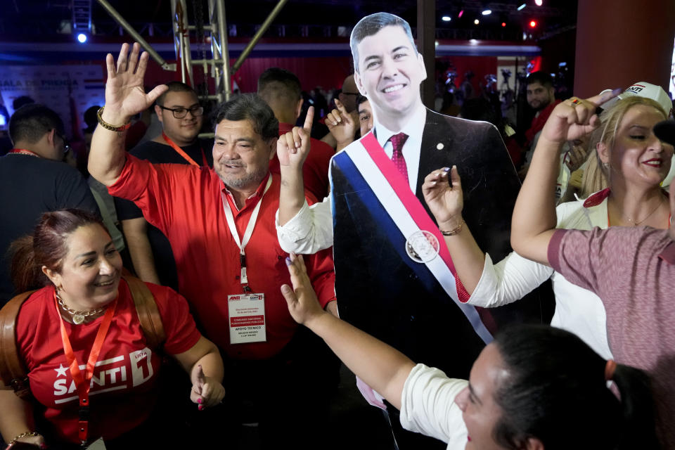 Seguidores de Santiago Peña, candidato presidencial del partido gobernante Colorado, reaccionan a los resultados parciales con una figura recortada de tamaño natural del candidato después del cierre de la votación durante las elecciones generales en Asunción, Paraguay, el domingo 30 de abril de 2023. (Foto AP/Jorge Sáenz)