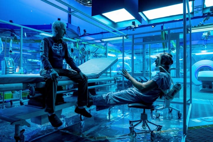 James Cameron sits on a desk discussing a shot with an actor during filming of Avatar: The Way of Water.