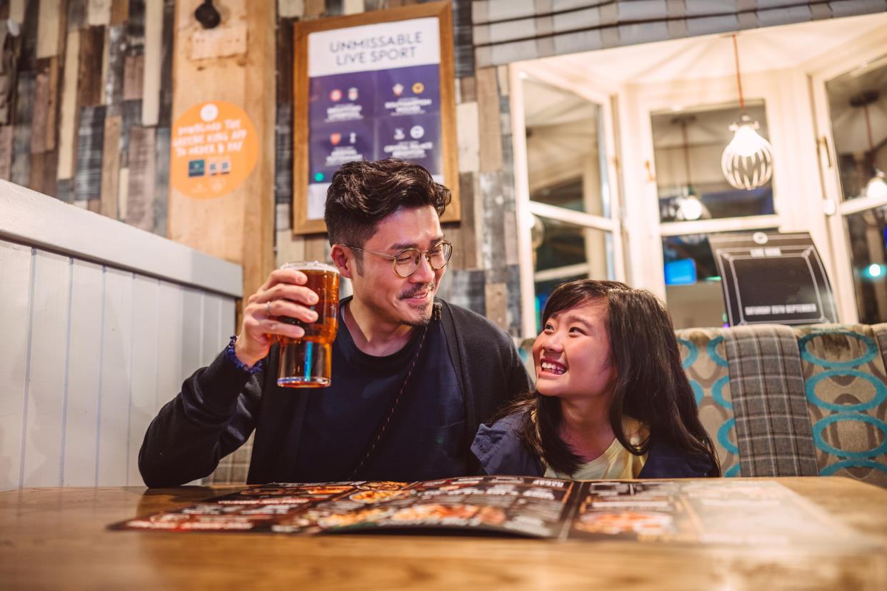 Young handsome dad enjoying a glass of beer, looking at food menu with his lovely daughter in restaurant joyfully.