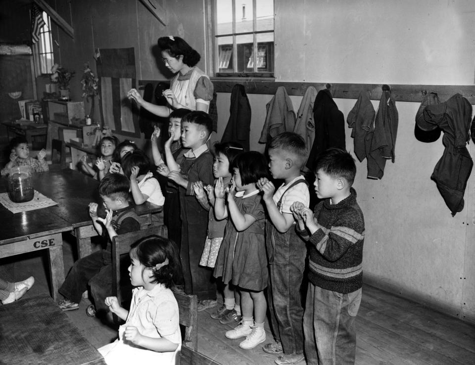 FILE - In this May 1943 file photo, Aiko Sumoge, an assistant teacher, leads a kindergarten class in singing an English folk song at the internment relocation center for Japanese Americans in Tulelake, Calif., during World War II. Beliefs that Hispanics and Asians living in the U.S. won't assimilate or refuse to speak English are based on stereotypes that scholars say are linked to notions of white supremacy. Throughout American history, Hispanics and Asians have been pressured to adopt the customs of the mainstream white population. The pressure came even as some laws forbade them from voting, intermarrying and having access to education and public facilities. (AP Photo, File)