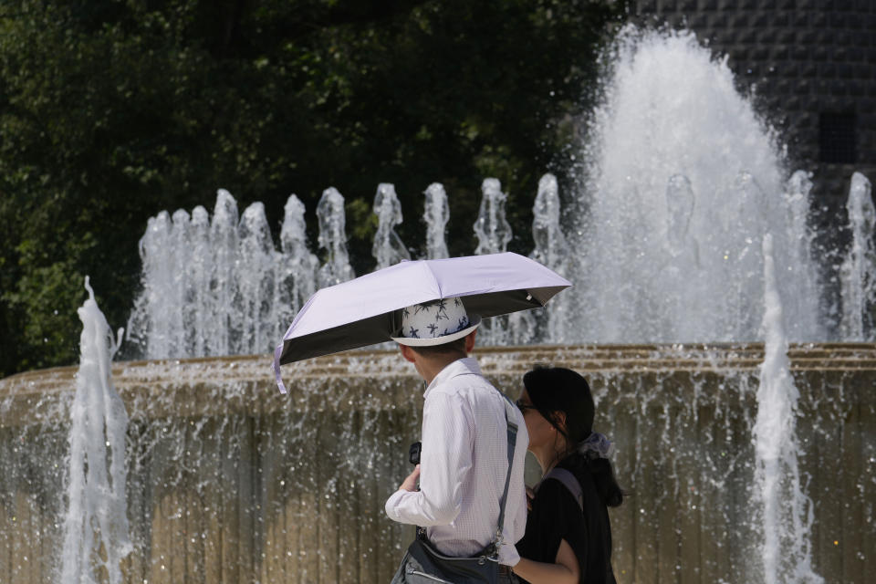 Tourists shelter from the sun as they pass by a fountain in front of the Sforzesco Castle in Milan, Italy, Thursday, July 11, 2024. A heat wave swept Italy on Thursday prompting health officials to issue a red alert for seven cities mostly in central Italy, including the capital Rome but also extending to the northern Adriatic city of Trieste on the border with Slovenia. (AP Photo/Luca Bruno)