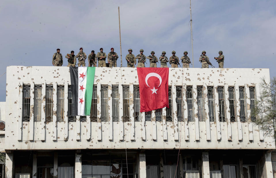 Turkish soldiers, right, and Turkey-backed opposition fighters stand atop a building next to their flags in Syrian town of Ras al Ayn, northeastern Syria, Wednesday, Oct. 23, 2019. Turkish media reports say Turkish troops and their allied Syrian opposition forces are securing a town in northeast Syria after Syrian Kurdish fighters pulled out of the area.(Ugur Can/DHA via AP)