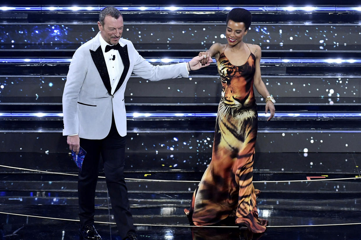 Lorena Monroe Cesarini, right, isa accompanied by Italian RAI State TV host Amadeus as she appears on the stage of the Ariston theater on the occasion of the Sanremo songs festival, in San Remo, Italy, Wednesday, Feb. 2, 2022. A Black Italian actress said she received on-line harassment after her appearance as a guest on Italy’s annual Sanremo music festival was announced. Lorena Monroe Cesarini told a live and TV audience on Wednesday that “evidently for someone, the color of my skin is a problem,” reading some messages she received on social media. They included messages saying she didn’t deserve being a guest at the music festival and that “they called you because you are black,” and one saying “maybe they called you to wash the staircase or put the flowers in vases.” (Matteo Rasero/LaPresse via AP)