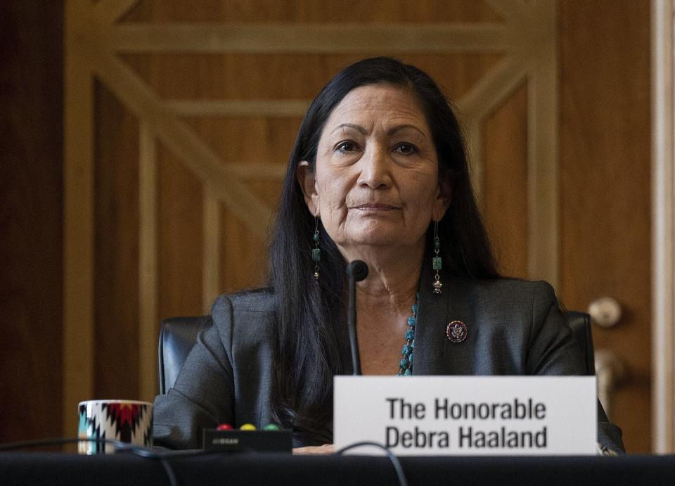 Deb Haaland sits behind a desk with a microphone