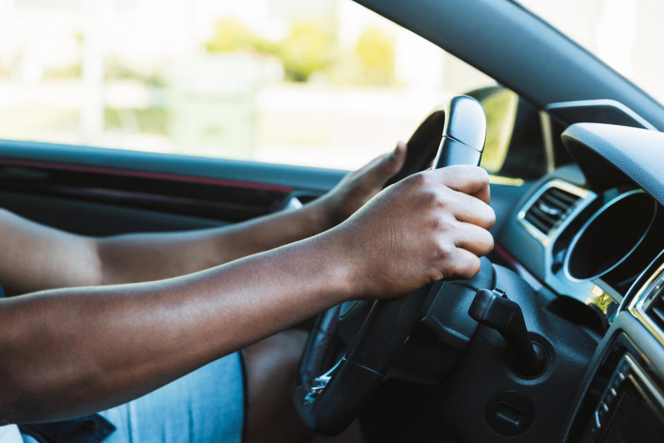 Sitting in the driver's seat of his car, the man grips the steering wheel.