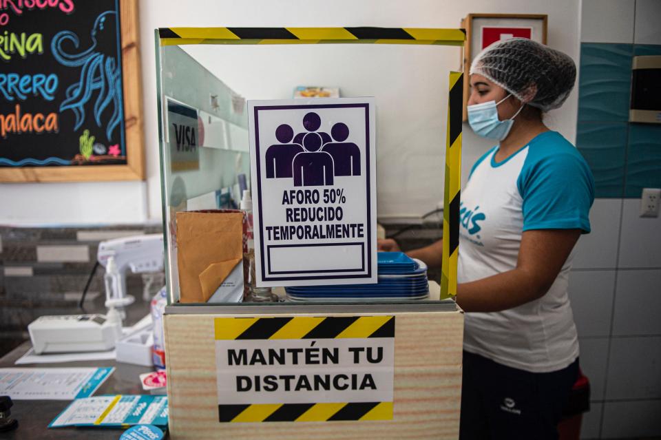 An employee stands next to a sign reading "Temporarily reduced capacity 50%" at a restaurant in Lima on July 20, 2020, mid the new coronavirus pandemic. - The restaurants of Peru, a country with world famous gastronomy, reopened their doors Monday after four months of confinement due to the new coronavirus pandemic, but hundreds did not manage to survive the quarantine. (Photo by ERNESTO BENAVIDES / AFP) (Photo by ERNESTO BENAVIDES/AFP via Getty Images)