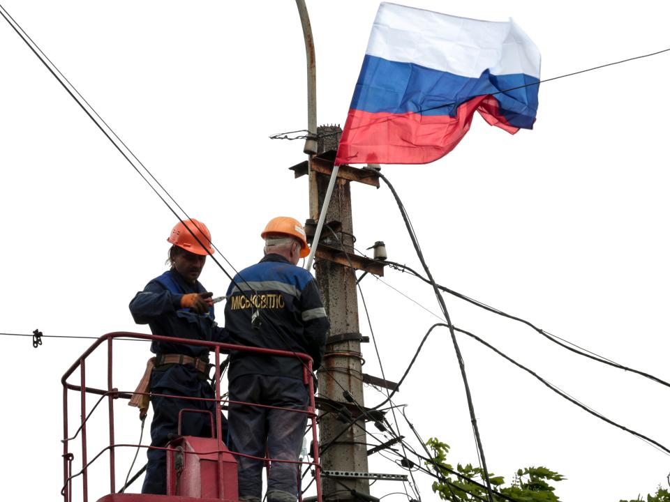 Municipal workers install a Russian flag on a pole.