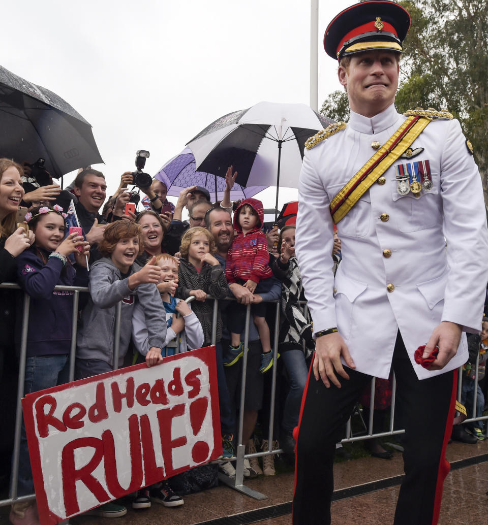 FILE - In this Monday, April 6, 2015 file photo, Britain's Prince Harry, right, reacts after shaking hands with kids holding up a sign reading "Red Heads Rule" during a visit to the Australian War Memorial in Canberra, Australia. Princess Diana’s little boy, the devil-may-care red-haired prince with the charming smile is about to become a father. The arrival of the first child for Prince Harry and his wife Meghan will complete the transformation of Harry from troubled teen to family man, from source of concern to source of national pride. (Lukas Coch, Pool Photo via AP, File)