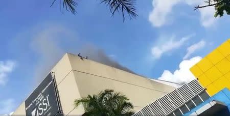 People are seen on the roof of a building as smoke rises during a fire in Davao, the Philippines, in this still image taken a December 23, 2017 social media video. Ashley Nicole Avila Rafaela/via REUTERS