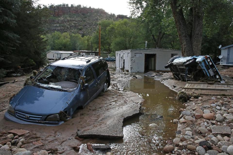 In this Sept. 13, 2013 file photo, cars lay mired in mud deposited by floods in Lyons, Colo. Little more than a year after Colorado Gov. John Hickenlooper assured the world his wildfire-ravaged state was still “open for business,” he may have to throw another lifeline to keep the state’s billion-dollar tourism industry afloat. (AP Photo/Brennan Linsley, File)