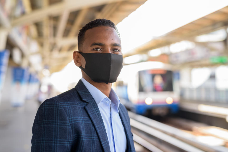 Portrait of young African businessman with mask for protection from corona virus outbreak at the sky train station