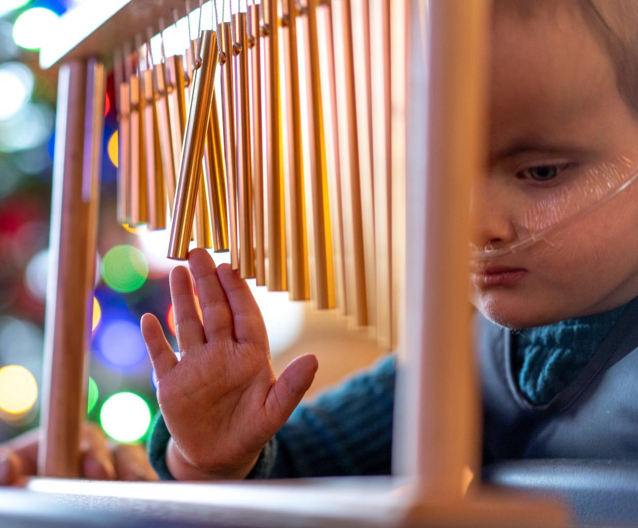 CC Calleja, 4, who was born with Trisomy 18, runs her hand on a set of chimes while in a stander to help with her leg strength, circulation and digestion in the living room of their home on Dec. 22, 2023.