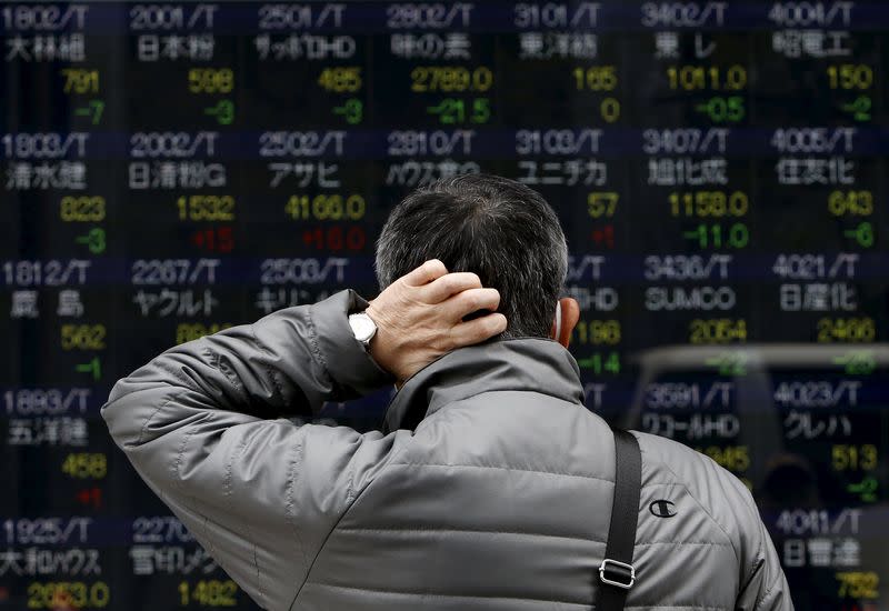 File photo of a pedestrian scratching his head looks at an electronic board showing the various stock prices outside a brokerage in Tokyo April 10, 2015. REUTERS/Yuya Shino