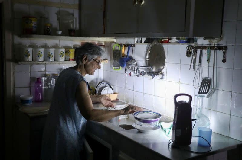 Samira Hanna, 70, washes dishes in her kitchen as she uses a portable electric light due to a power cut, in Beirut