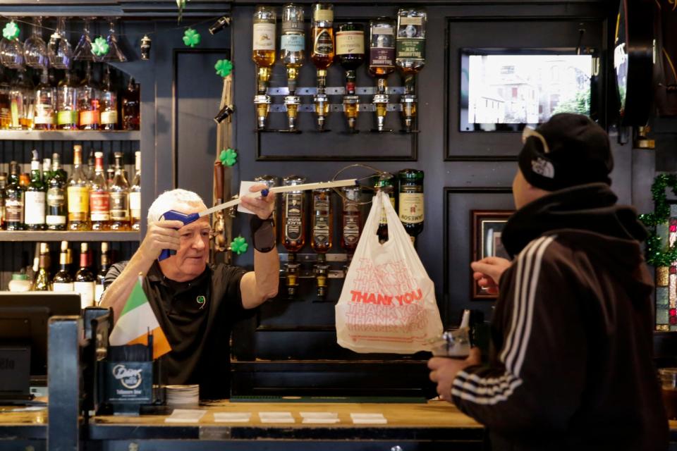 Owner Jerry O'Bryan hands a customer their order from behind the Nine Irish Brothers bar, Tuesday, March 17, 2020, in West Lafayette.