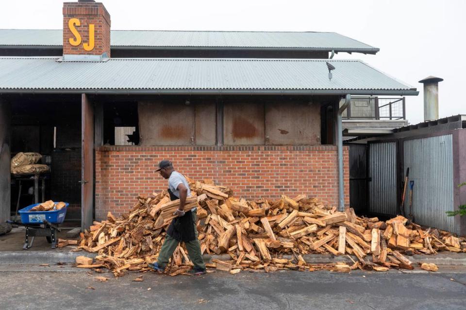 Pitmaster Alonzo Blackledge moves wood inside the cook house to protect it from the rain, so they will have dry wood to start the fire in the morning at Sam Jones BBQ on Wednesday, August 30, 2023 in Winterville, N.C.