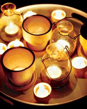 Cluster candles on a tray, using a variety of vessels, including terra cotta pots.