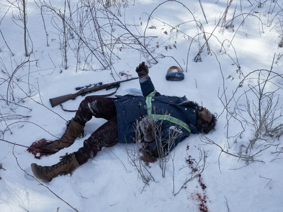 jeevan lying in the snow in station eleven, a gun and hat lying by his side and a trail of blood leading to his body