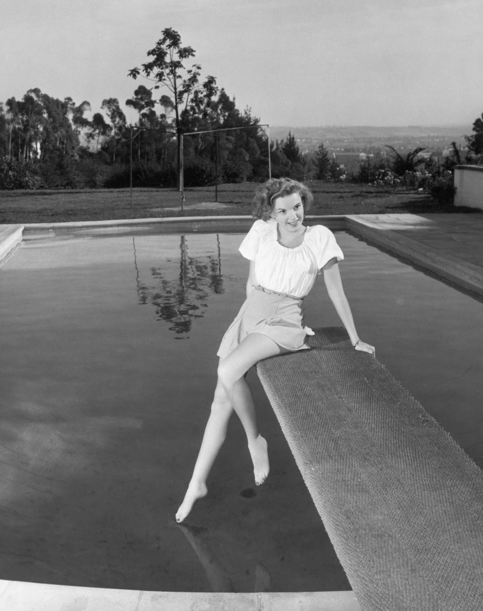 Garland is wearing a short skirt and blouse on the diving board of an outdoor swimming pool in this undated photo.