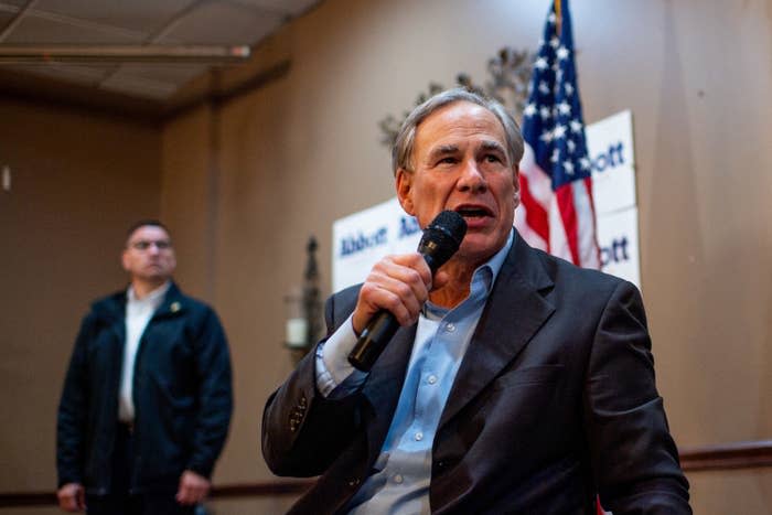 Abbott speaks into a microphone while sitting down with an American flag behind him