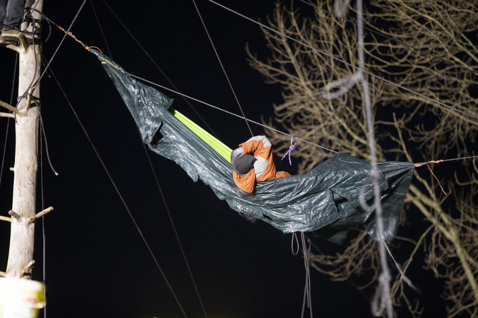 A climate activist lies in a kind of hammock between trees in the activists' camp, in Luetzerath, Germany, Wednesday, Jan. 11, 2023. Environmental activists have been locked in a standoff with police who started eviction operations on Wednesday in the hamlet of Luetzerath, west of Cologne, that's due to be bulldozed for the expansion of a nearby lignite mine. (Thomas Banneyer/dpa via AP)