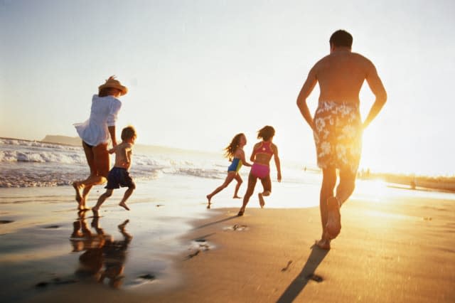 Family running on beach at sunset, rear view