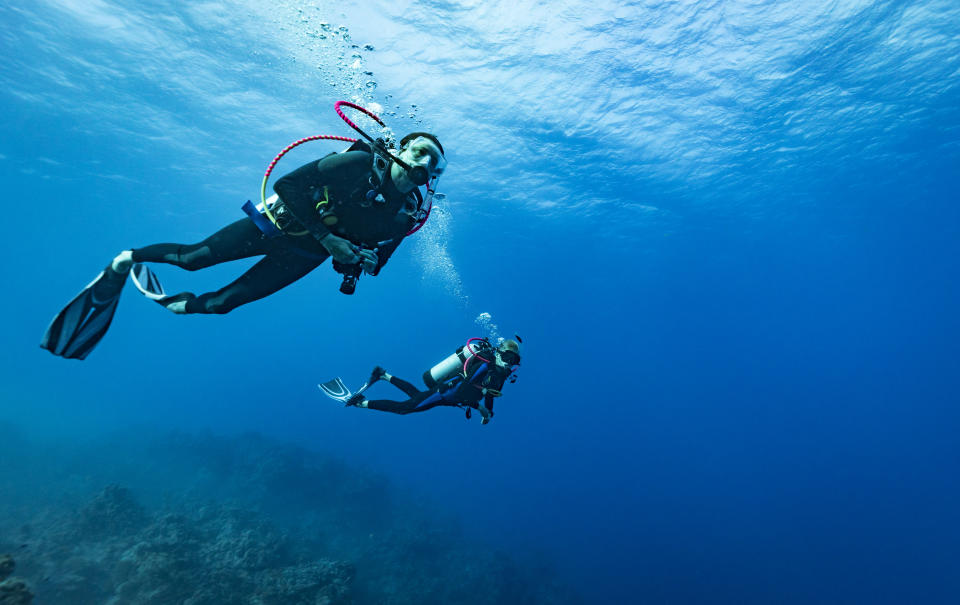 Two scuba divers swim underwater with full gear and oxygen tanks, surrounded by a clear, deep ocean
