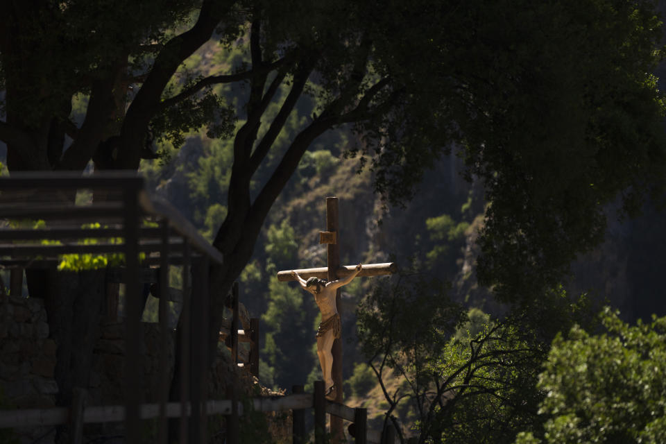 A cross with a statue of a crucified Jesus Christ hidden between the trees in the Saint Elisha Monastery, hidden in the scenic Kadisha Valley, a holy site for Lebanon's Maronite Christians, in the northeast mountain town of Bcharre, Lebanon, Saturday, July 22, 2023. For Lebanon's Christians, the cedars are sacred, these tough evergreen trees that survive the mountain's harsh snowy winters. They point out with pride that Lebanon's cedars are mentioned 103 times in the Bible. (AP Photo/Hassan Ammar)