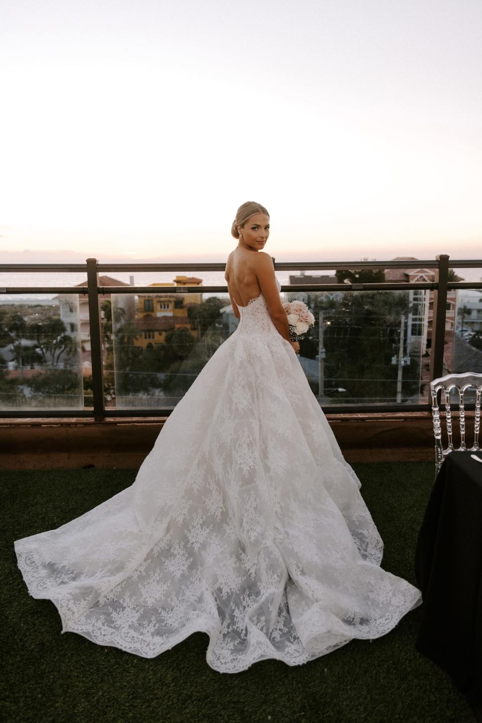 A bride smiles over her shoulder as she leans on a railing in front of the sunset.