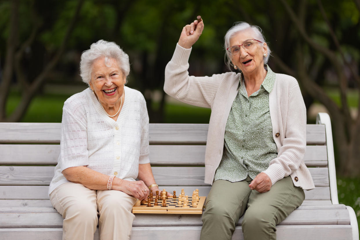 pension  Elderly best friends playing chess in public park, sitting on the park bench. Senior women enjoying free time, having fun together. Two female residents playing chess in nursing home garden. Concept of friendship and free time activities in retirement.