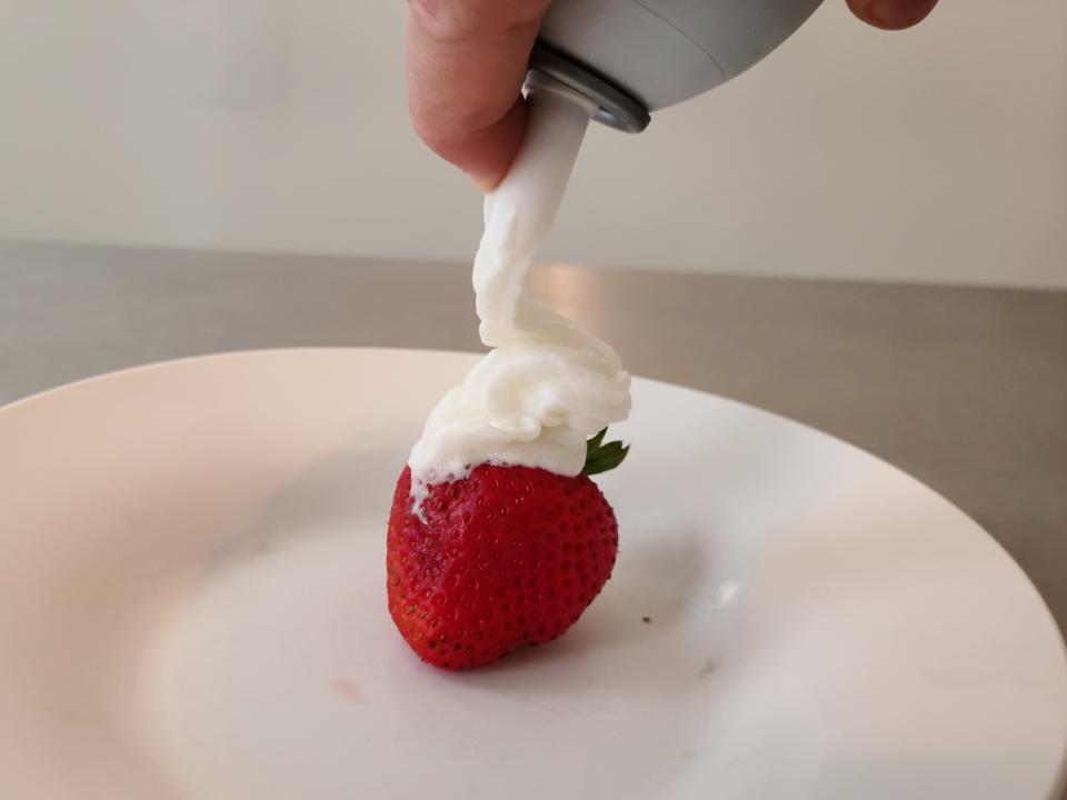 hand spraying whole foods whipped cream onto a strawberry