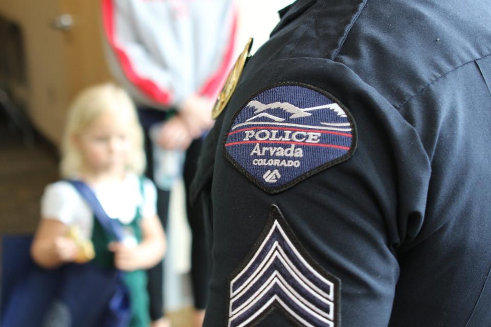 An Arvada police officer is pictured with a child in the background.