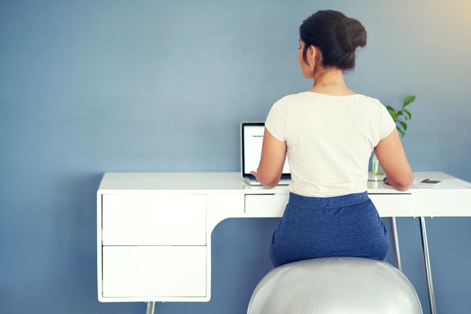 A woman sits on a flexible ball to work at her desk