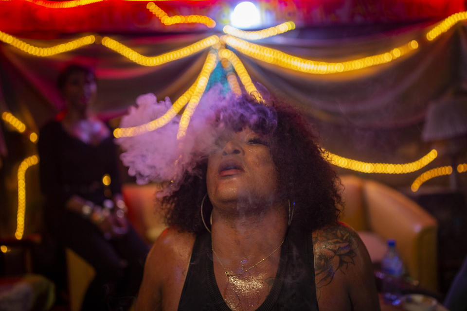 Laurent Voltus, que vive en el centro Kay Trans Haití, exhala el humo de un cigarrillo mientras baila con amigos en un club, en Puerto Príncipe, Haití, el 18 de agosto de 2020. Los residentes del centro pueden llevar a sus parejas a las instalaciones, ir a clubes y a comprar sin el miedo a ser tratados mal por los comerciantes del vecindario, que son cada vez más amables y acogedores. (AP Foto/Dieu Nalio Chery)