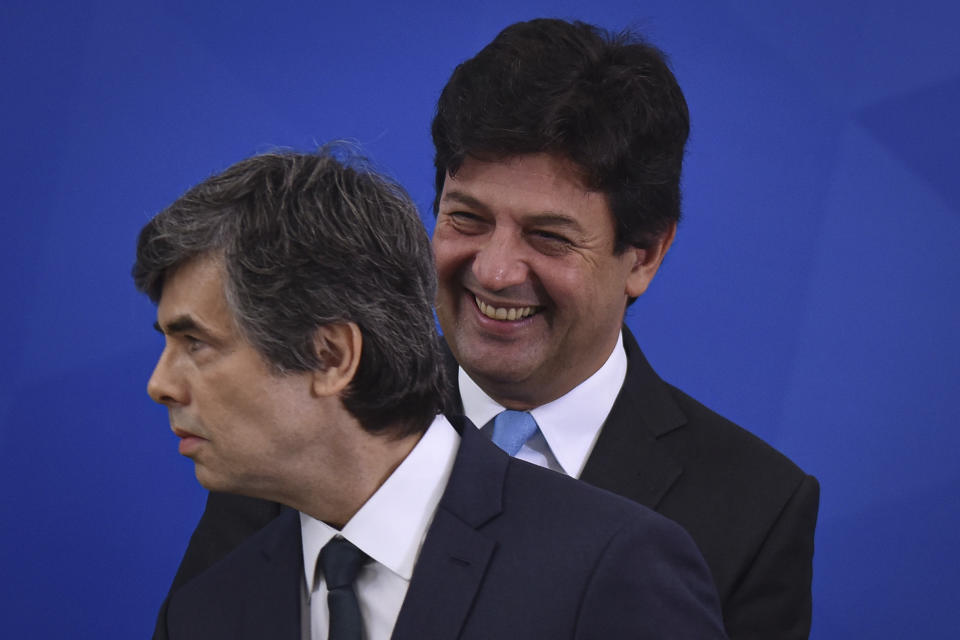 Brazil's outgoing Health Minister Luiz Henrique Mandetta, behind, smiles behind his replacement Nelson Teich at a swearing-in ceremony in Planalto Palace, Brasilia, Brazil, Friday, April 17, 2020. (AP Photo/Andre Borges)