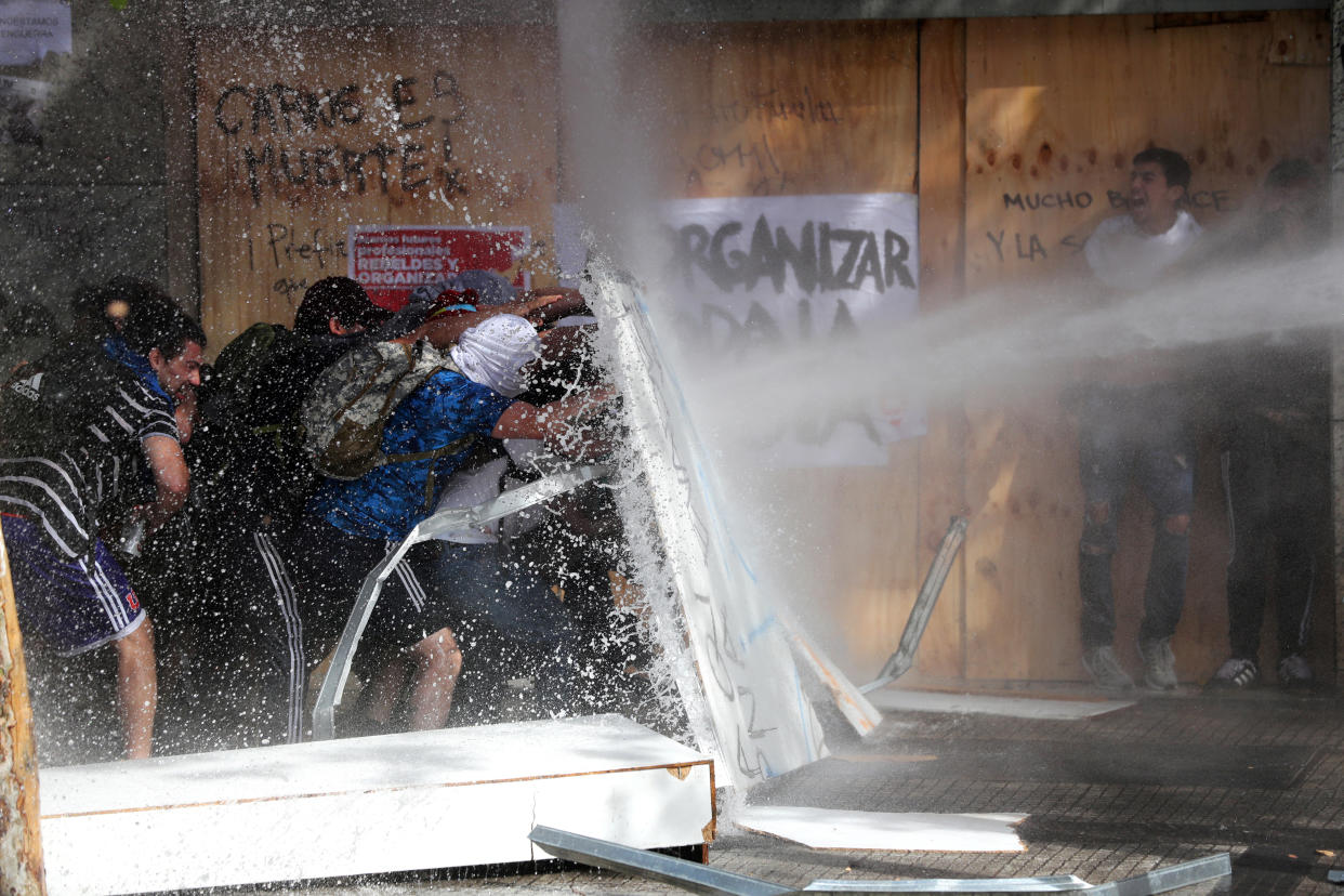 Demonstrators take cover as they are sprayed by security forces with a water cannon during a protest against Chile's state economic model in Santiago, Chile on Oct. 23, 2019. (Photo: Ivan Alvarado/Reuters)